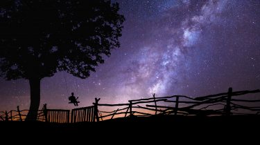 A silhouette of a child on a swing looking at the stars