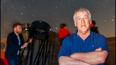 Mike Simmons with a telescope and stargazers in the background looking at the night's sky